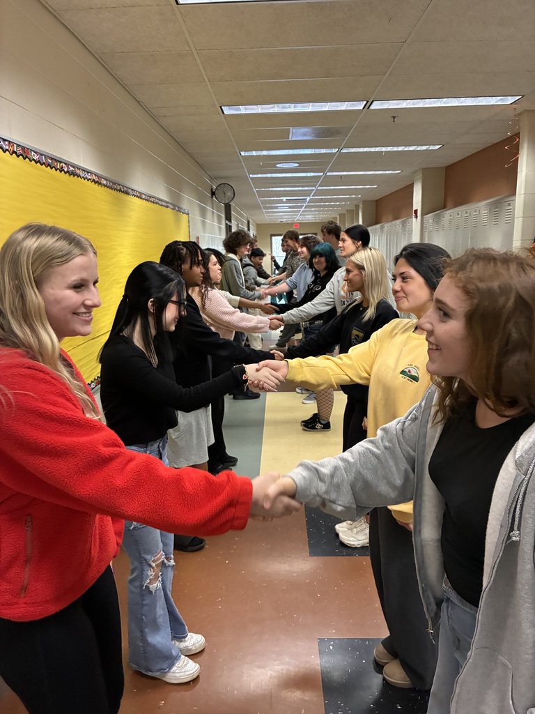 Students work in pairs to practice handshake skills in a school hallway.