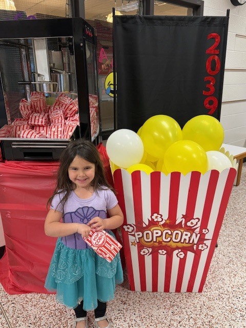 A child poses for a photo in front of a kindergarten registration day backdrop.