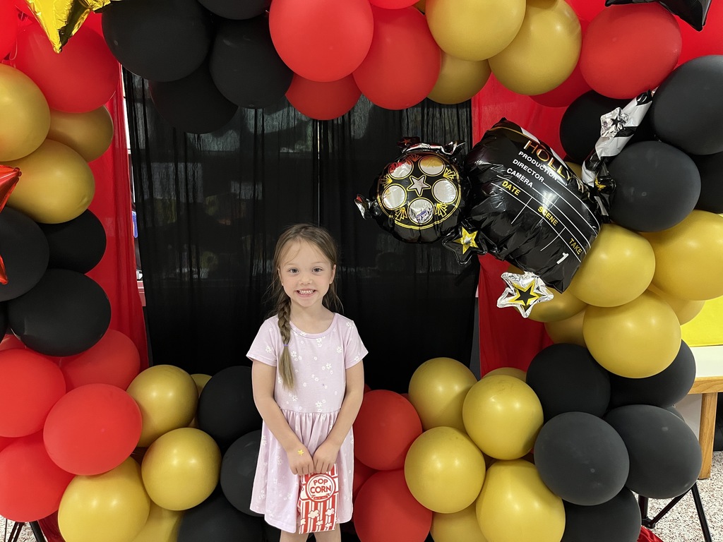 A child poses for a photo in front of a kindergarten registration day backdrop.