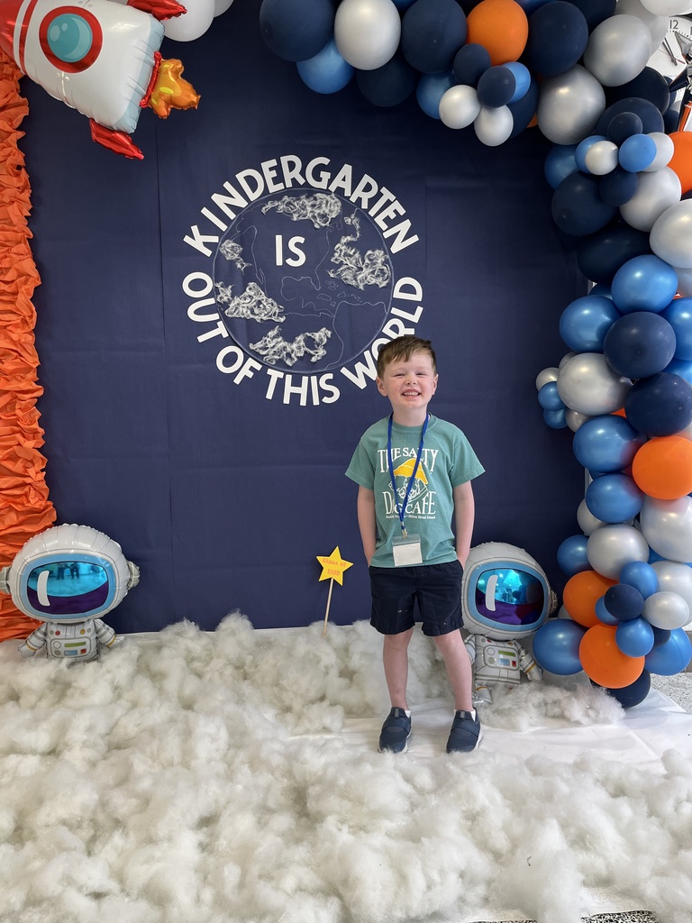 A child poses for a photo in front of a kindergarten registration day backdrop.