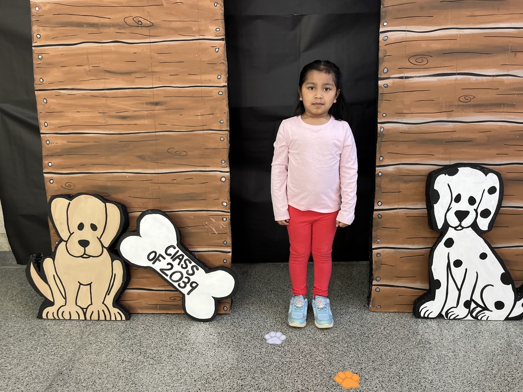 A child poses for a photo in front of a kindergarten registration day backdrop.