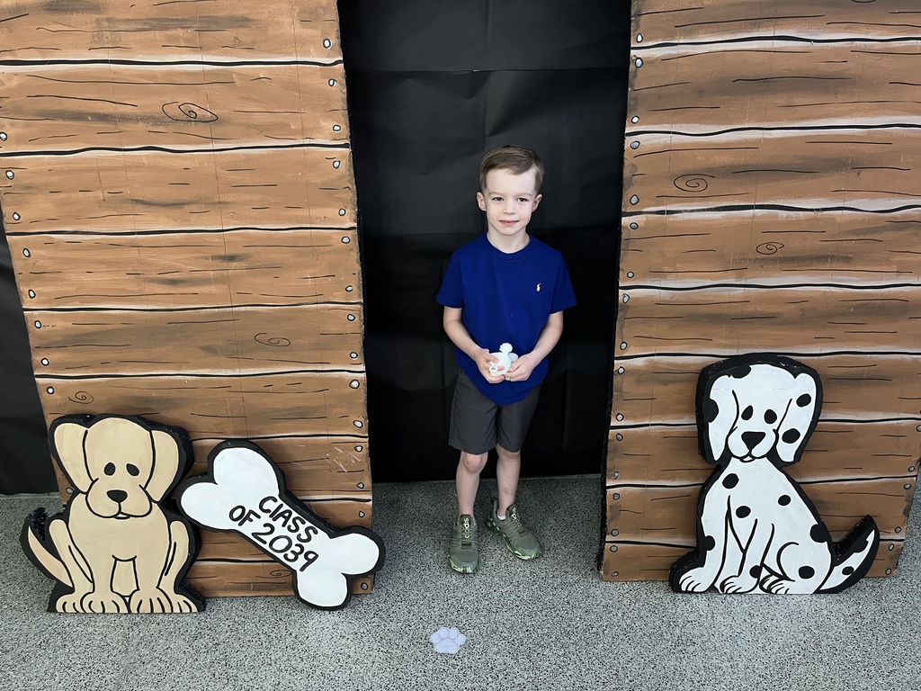 A child poses for a photo in front of a kindergarten registration day backdrop.
