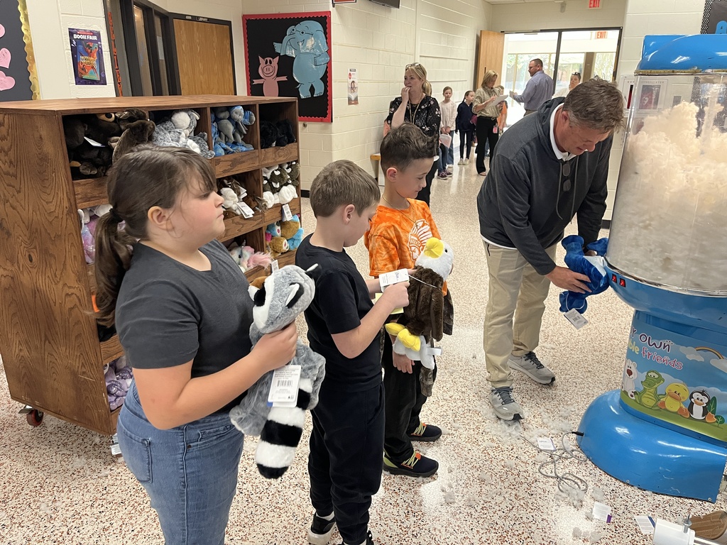 A man uses a machine to fill a stuffed animal for a waiting child. Other children wait in line.