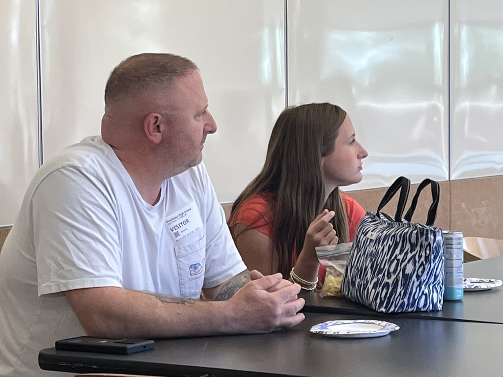 A man and teen listen to a speaker.