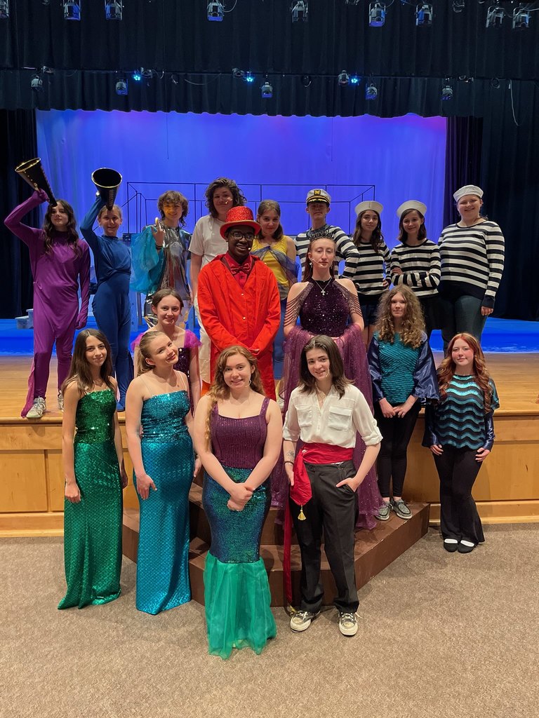 Eighteen teenagers dressed in costume as the cast of The Little Mermaid pose on a stage for a cast photo.