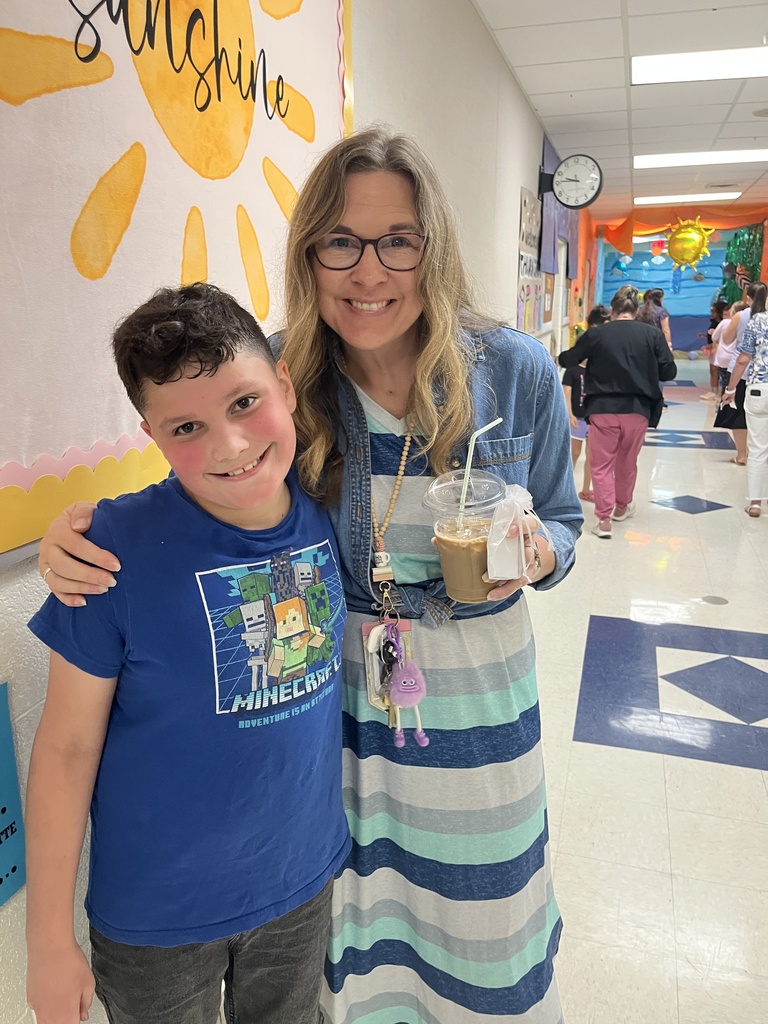 A teacher holding a drink poses with a student.