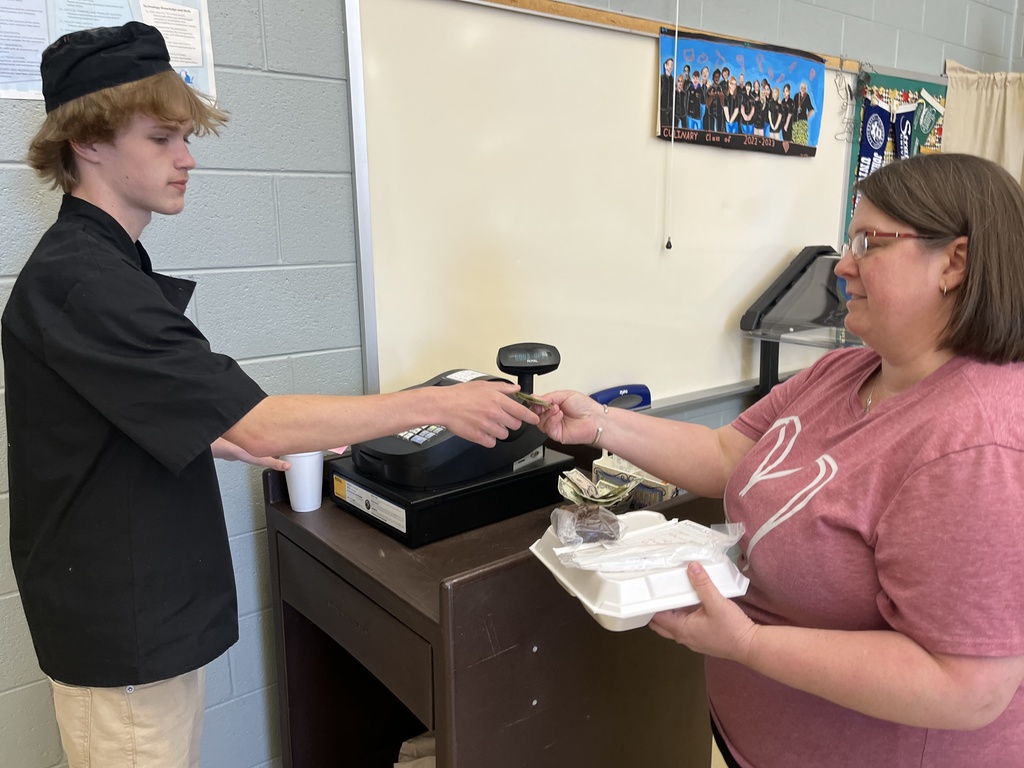 A teacher pays for her meal in a culinary cafe, giving the money to a student cashier.