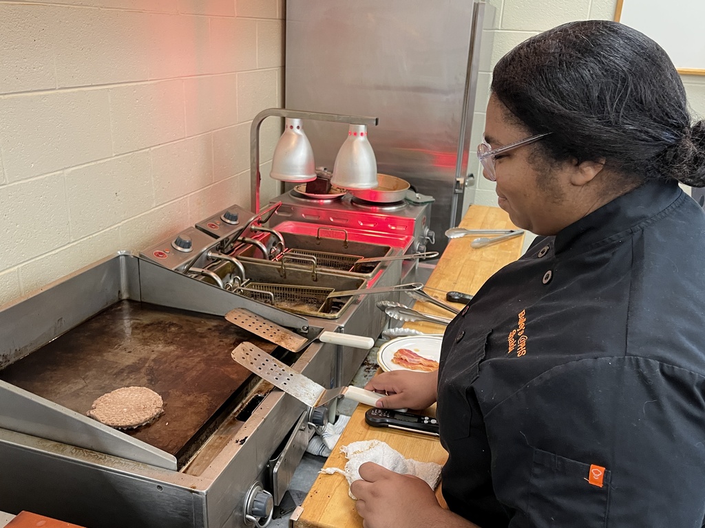 A student cook heats a hamburger on a grill. 