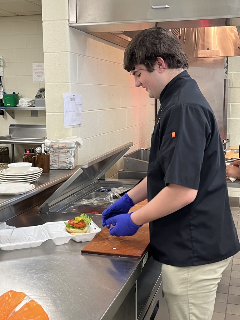 A student cook makes a hamburger.