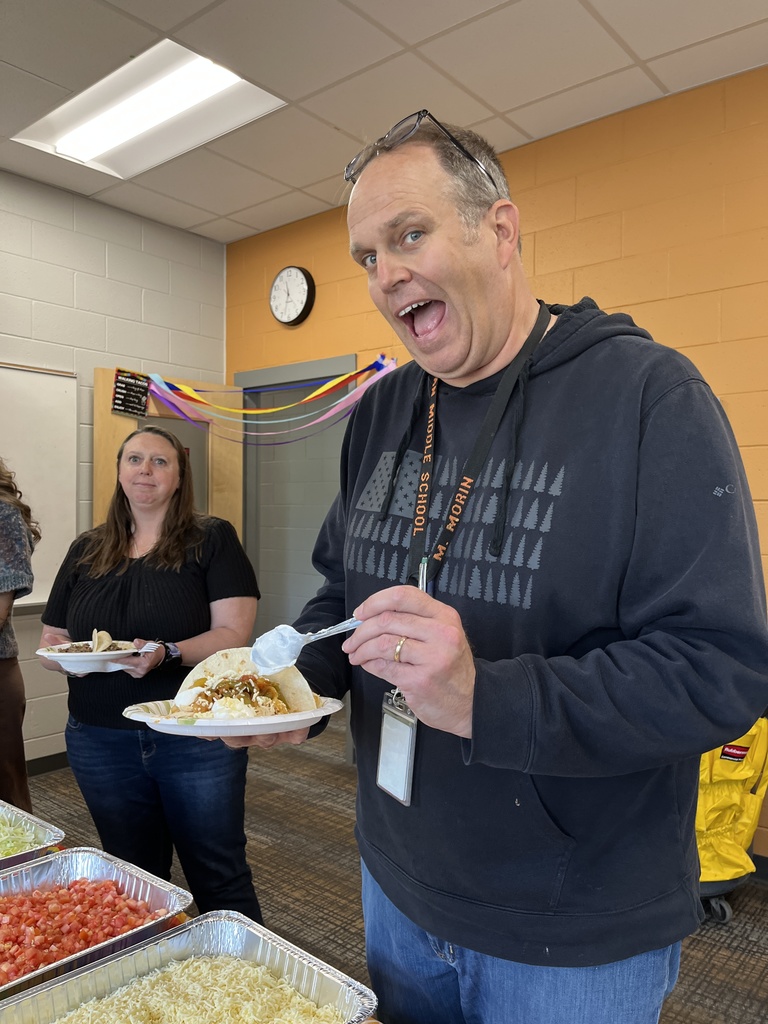 Two staff members pose for a photo at a staff appreciation taco bar at a school.
