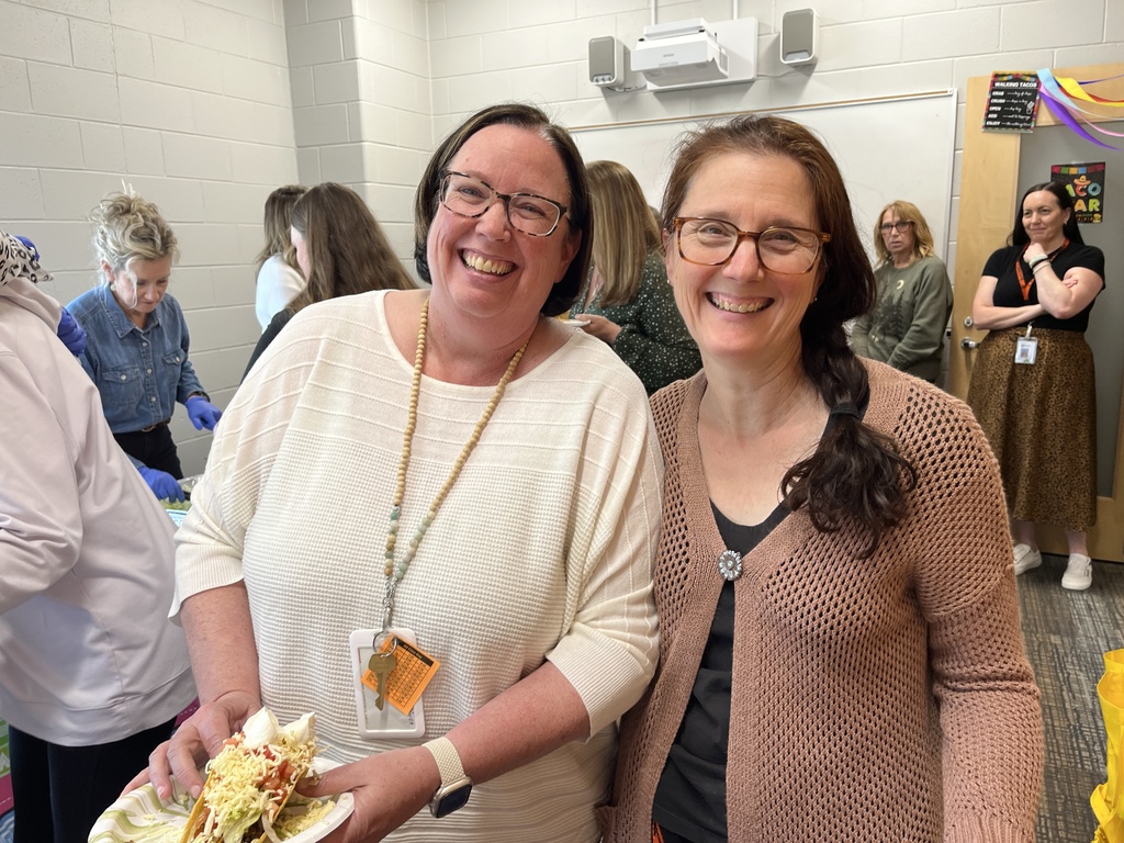 Two staff members pose for a photo at a staff appreciation taco bar at a school.