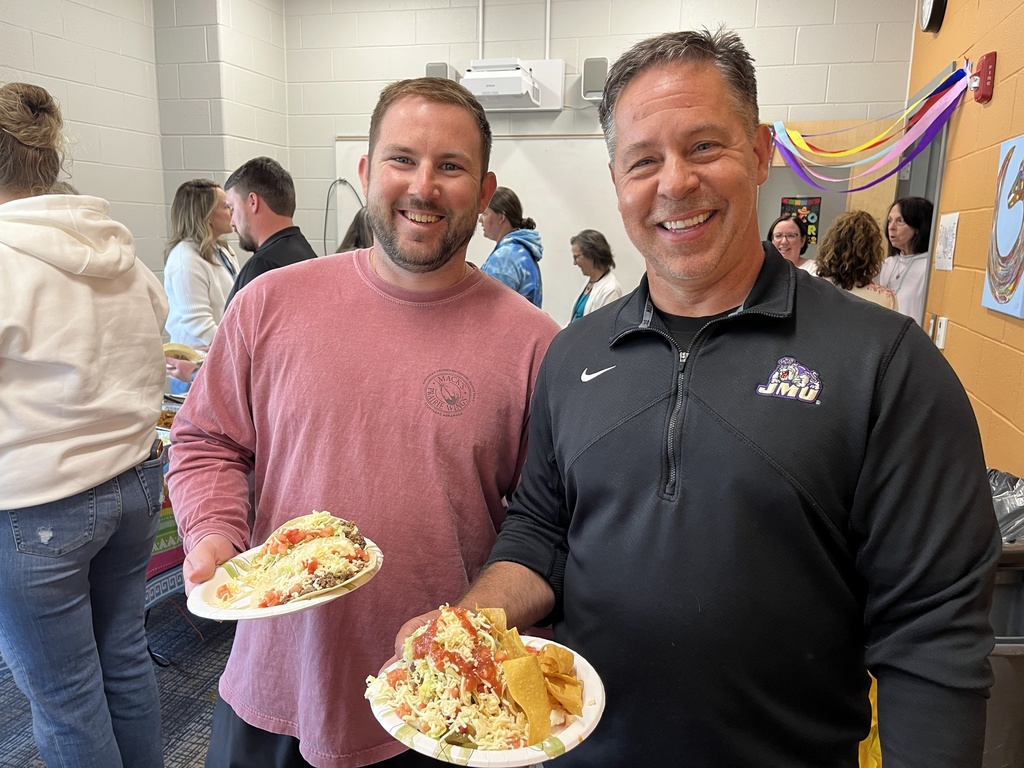 Two staff members pose for a photo at a staff appreciation taco bar at a school.