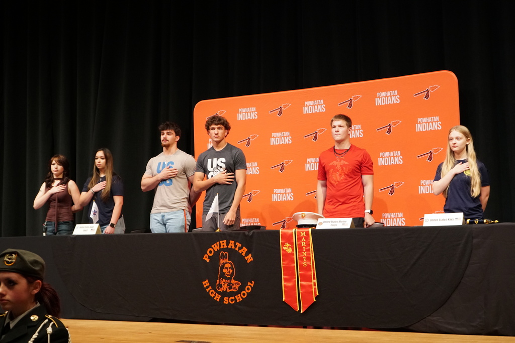 High school students stand for the pledge of allegiance at a military signing day ceremony.