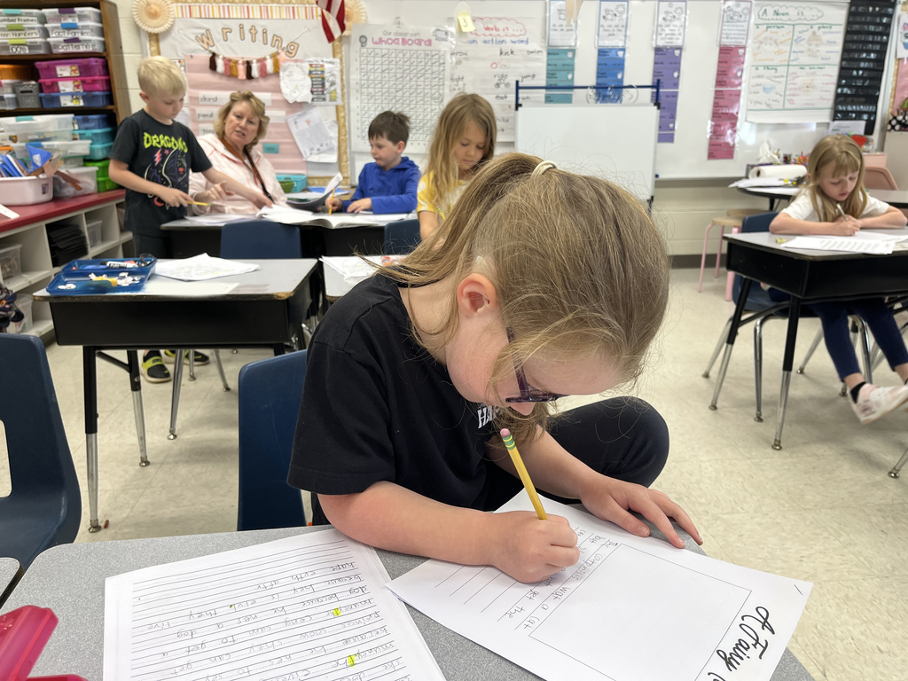 First graders in class work on a fairy tale assignment. A teacher helps one student.