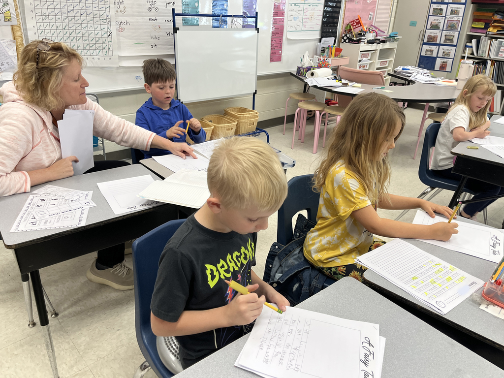 First graders in class work on a fairy tale assignment. A teacher helps one student.