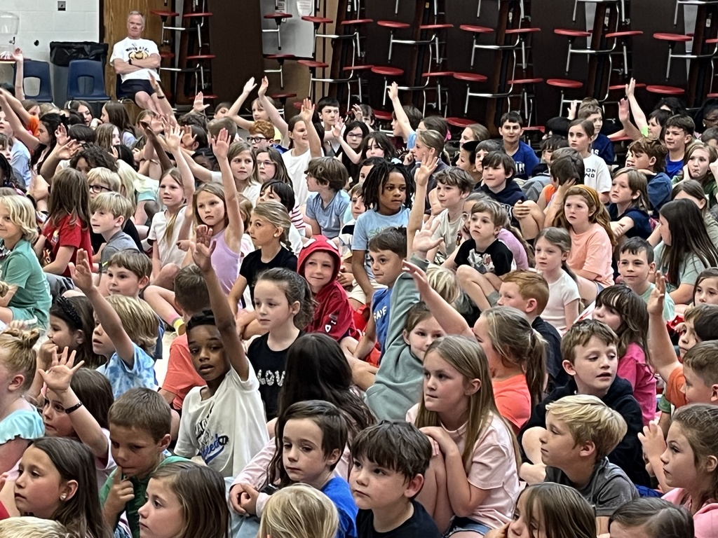 Photo of a cafeteria full of children sitting down and watching an event on stage. 