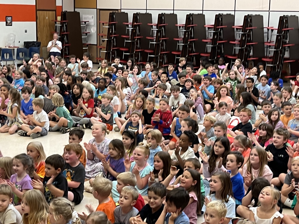 Photo of a cafeteria full of children sitting down and watching an event on stage. 