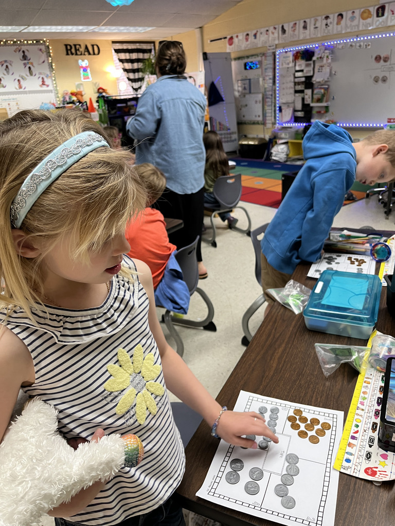 Kindergartners learns about the value of money by working with replica coins. A teacher helps one of the students.