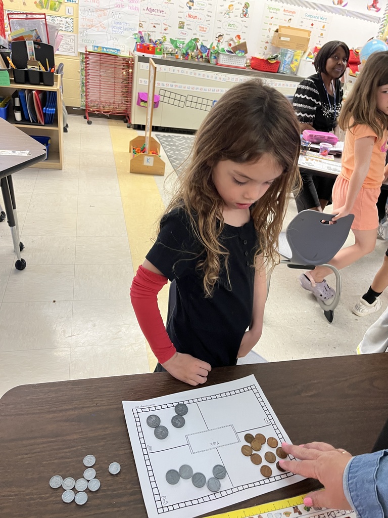 Kindergartners learns about the value of money by working with replica coins. An adult helps one of the students.