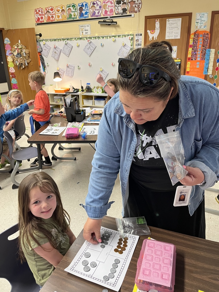 Kindergartners learns about the value of money by working with replica coins. A teacher helps one of the students.