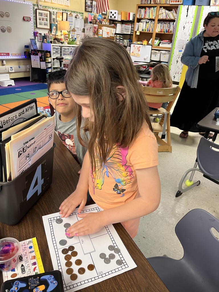 Kindergartners learns about the value of money by working with replica coins. A teacher helps one of the students.