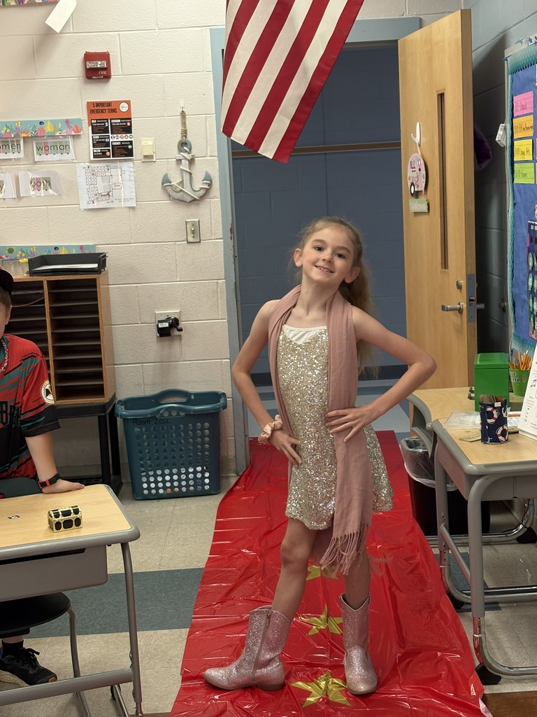 A student enters a classroom decorated for a Hollywood theme day and poses on the red carpet.
