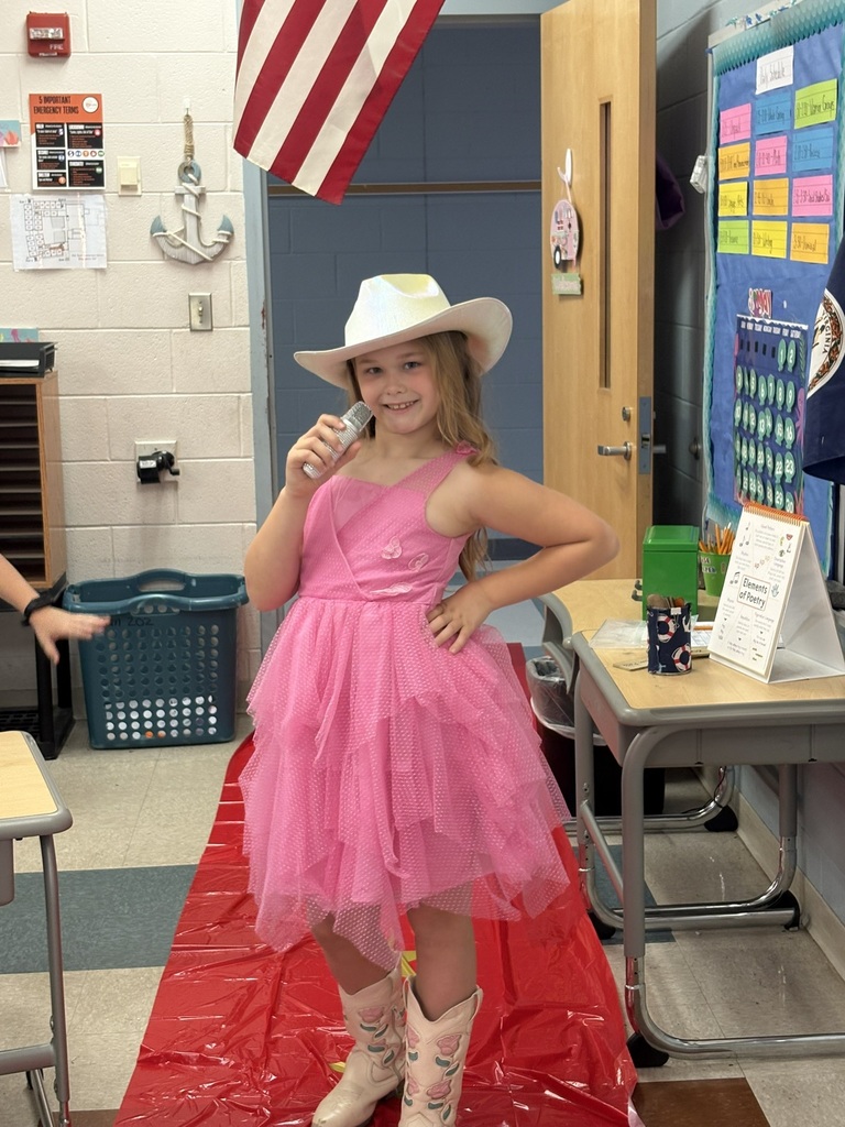 A student enters a classroom decorated for a Hollywood theme day and poses on the red carpet.