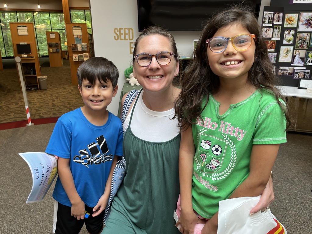 An adult and two children pose for a photo at a summer reading program kickoff event.