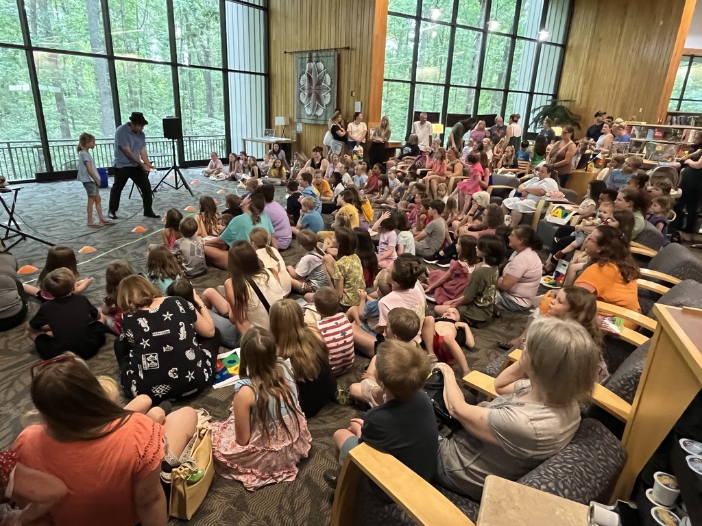 A juggler performs for a large group of adults and children at a summer reading kickoff event.
