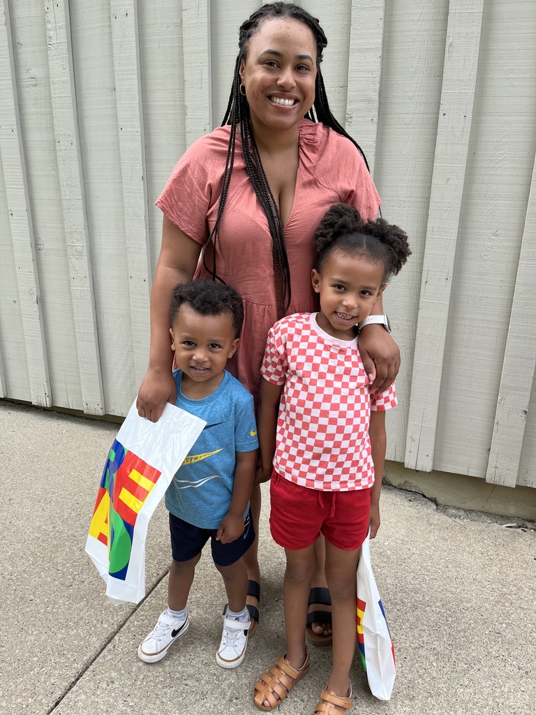 An adult and two children pose for a photo at a summer reading program kickoff event.