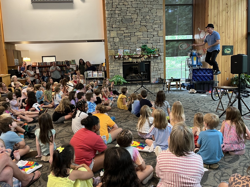 A juggler performs for a large group of adults and children at a summer reading kickoff event.