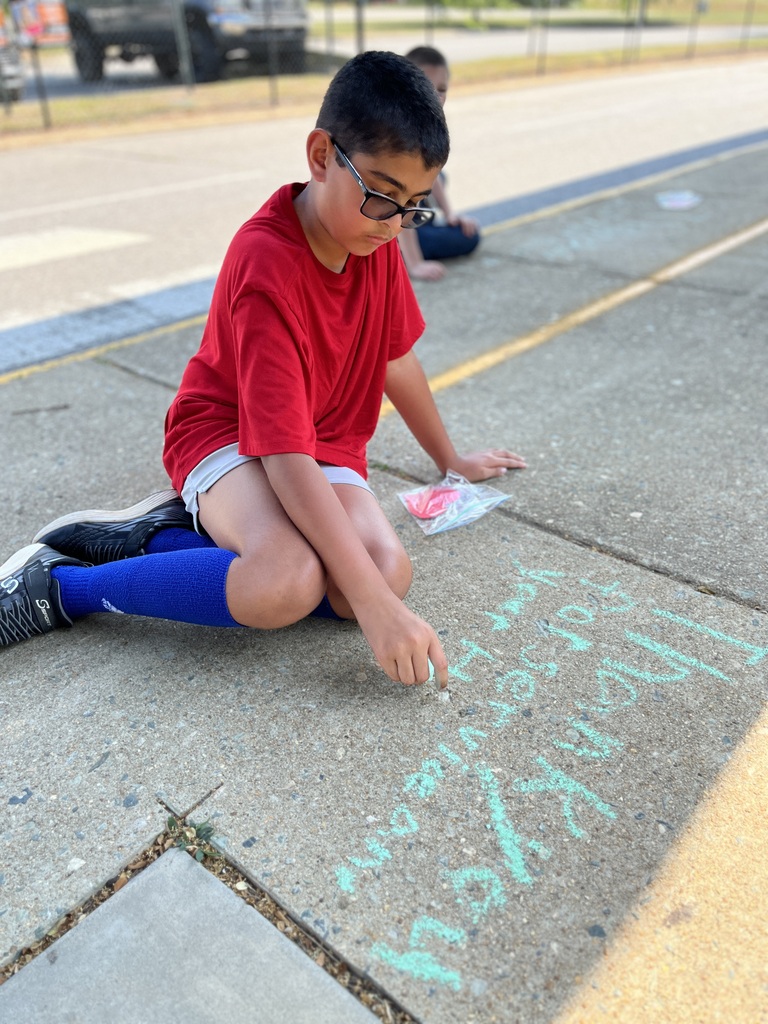 A students sit on the ground making a chalk tribute during a Memorial Day ceremony.