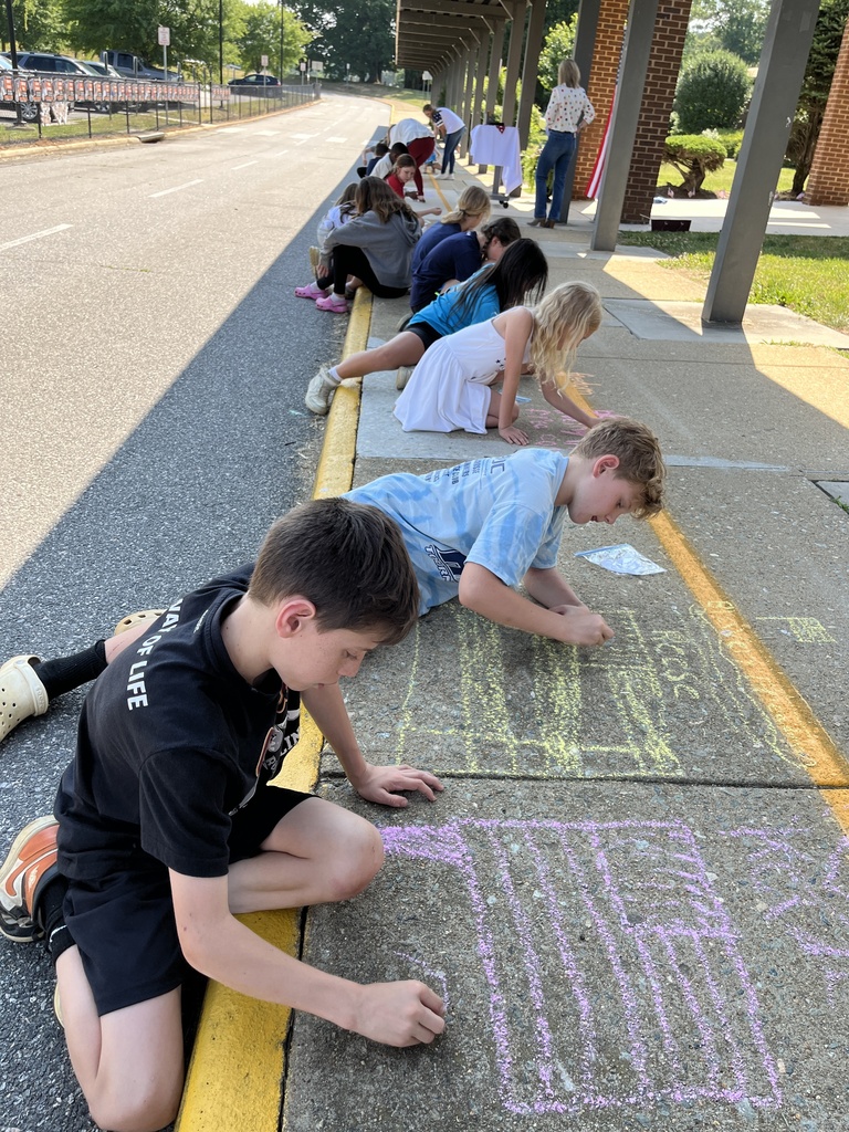 Students sit on the ground making a chalk tribute during a Memorial Day ceremony.