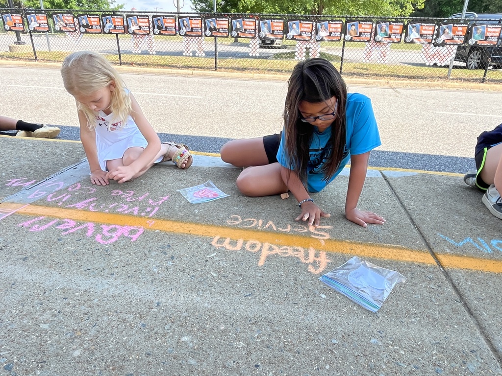 Students sit on the ground making a chalk tribute during a Memorial Day ceremony.