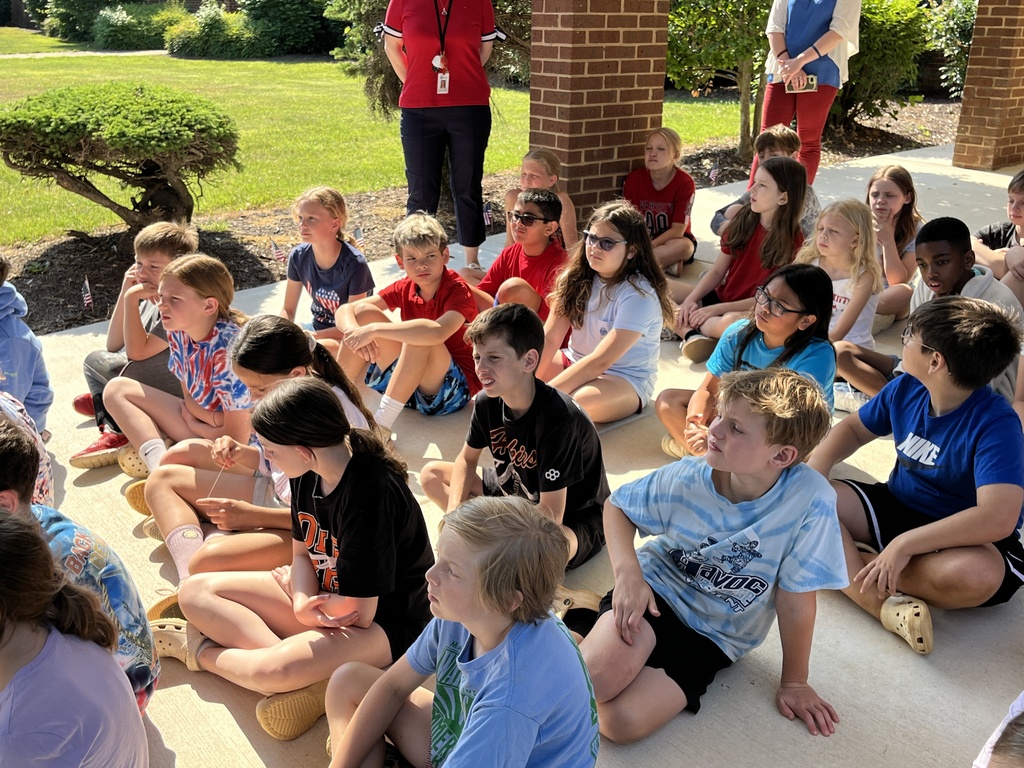 Students sit on the ground listening during a Memorial Day ceremony.