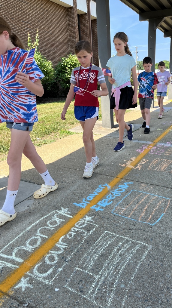 Students walk in a line looking at a chalk tribute during a Memorial Day ceremony.