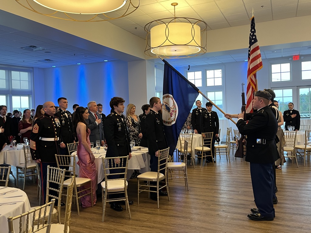 A room full of people stand for the presenting of the colors during a JROTC military ball.
