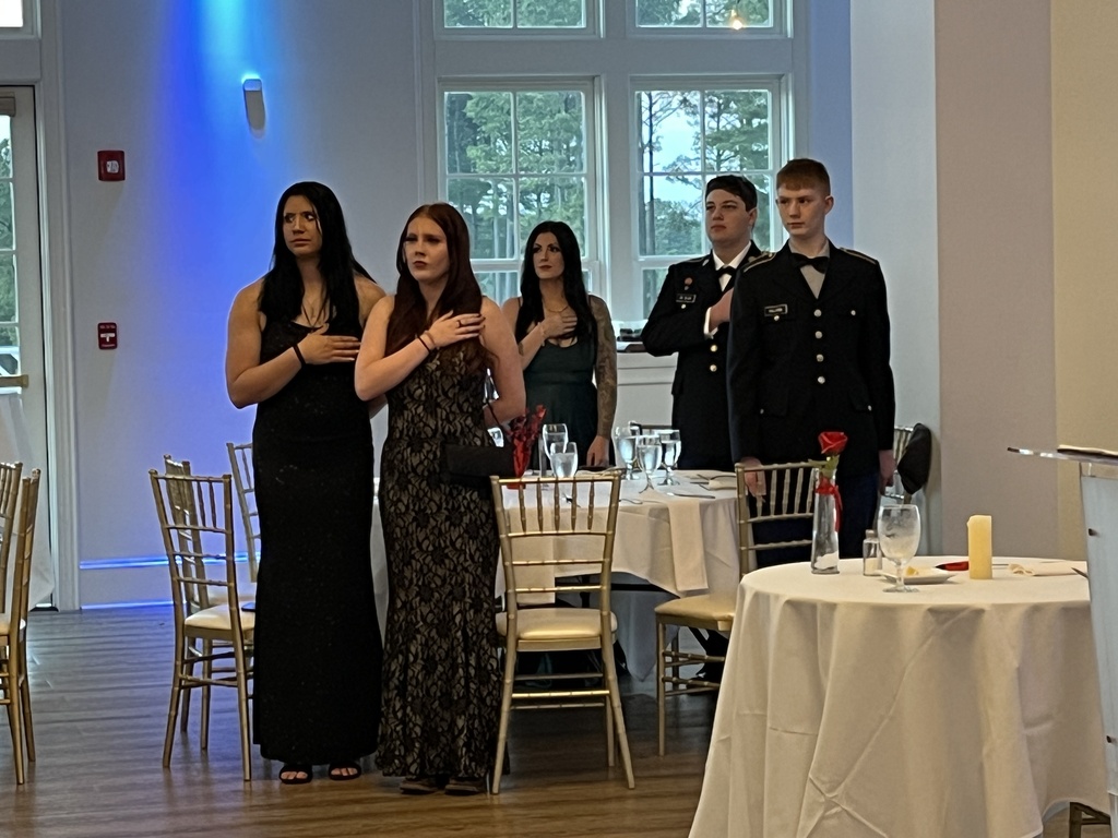 A group of students in formal dress stand for the presenting of the colors during a JROTC military ball.