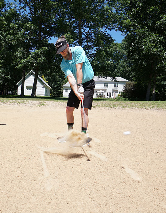 A golfer takes his shot with a golf club in a sand trap during a golf tournament. 