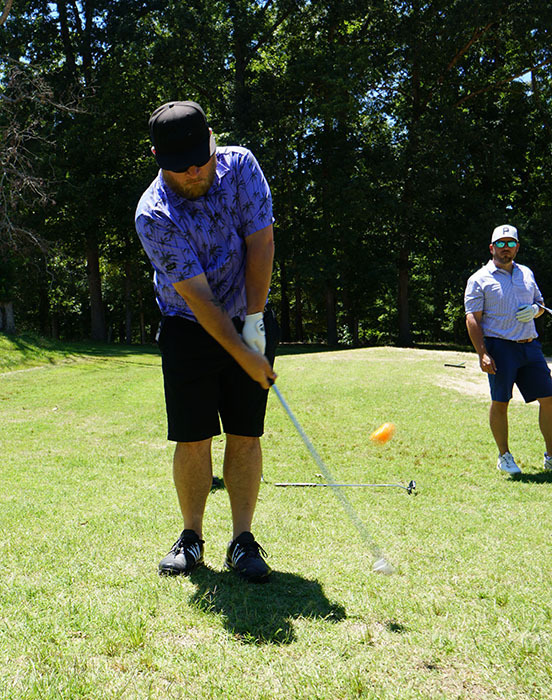 A golfer takes his shot with a golf club during a golf tournament.  A teammate watches.