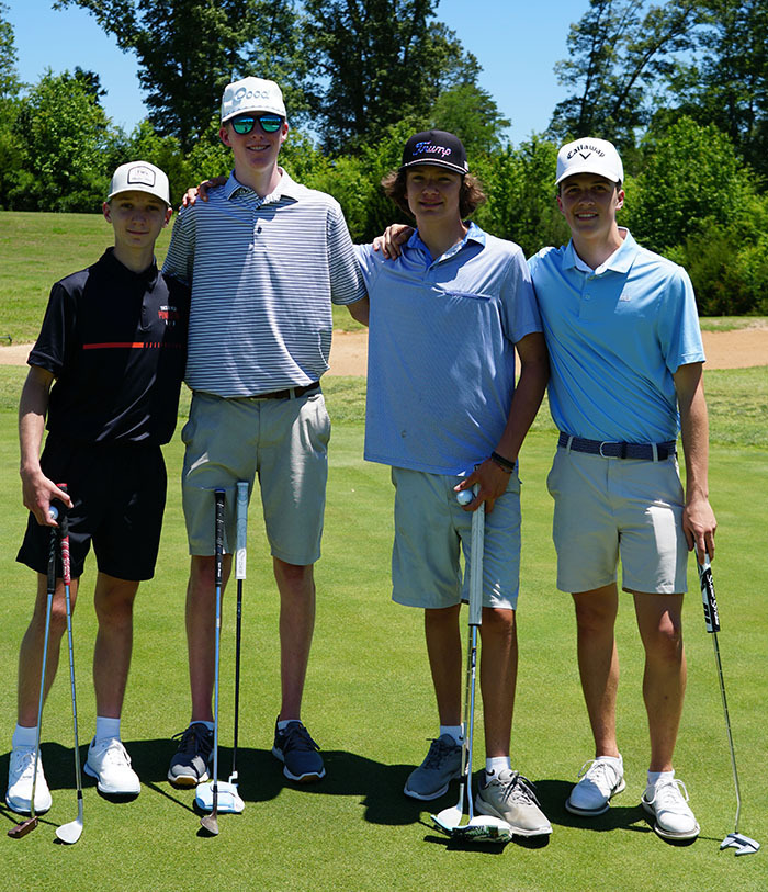 A 4-person student team poses for a photo on the golf course during a golf tournament. 