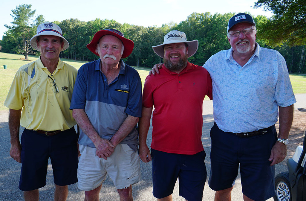 The winning 4-person team poses for a photo at the end of a golf tournament. 