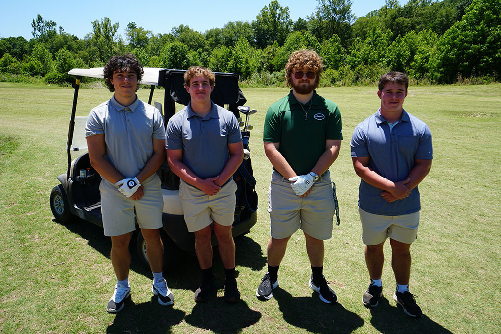 A 4-person student team poses for a photo on the golf course during a golf tournament. 