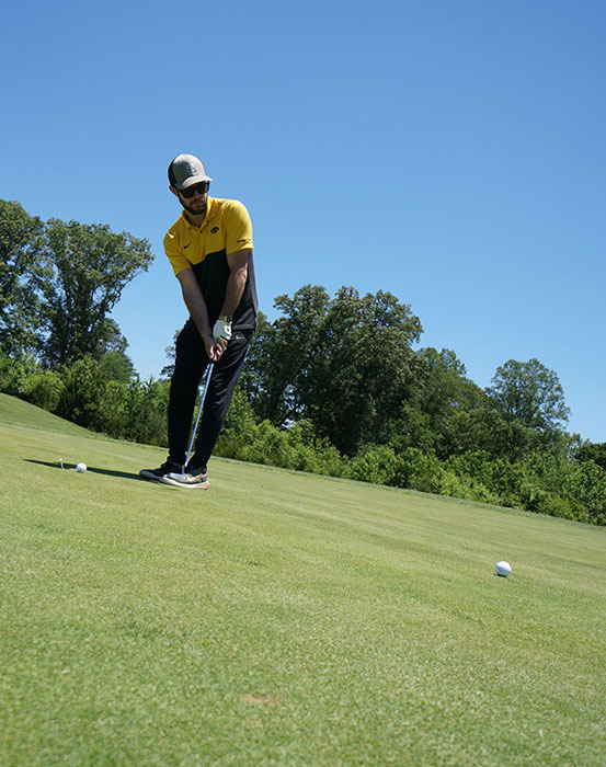 A golfer takes his shot with a golf club during a golf tournament. 