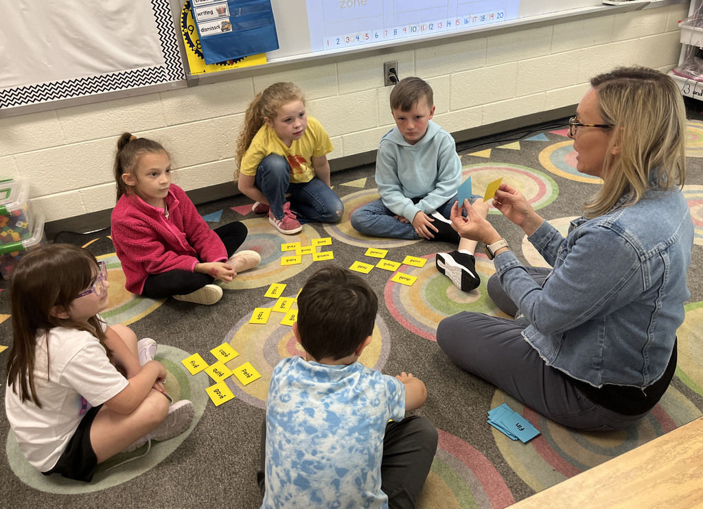 Students work at a literacy station with their teacher to practice long vowel sounds .