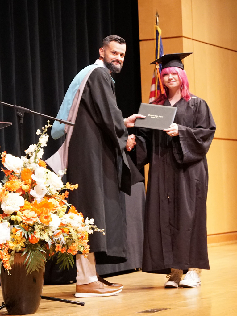 A graduate accepts her diploma from the high school principal during a summer graduation.