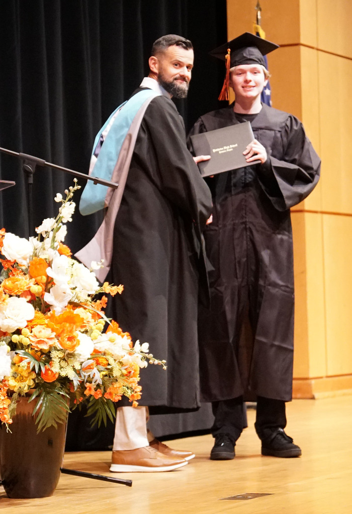 A graduate accepts his diploma from the high school principal during a summer graduation.