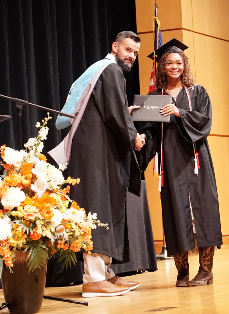 A graduate accepts her diploma from the high school principal during a summer graduation.