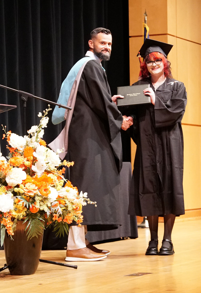 A graduate accepts her diploma from the high school principal during a summer graduation.