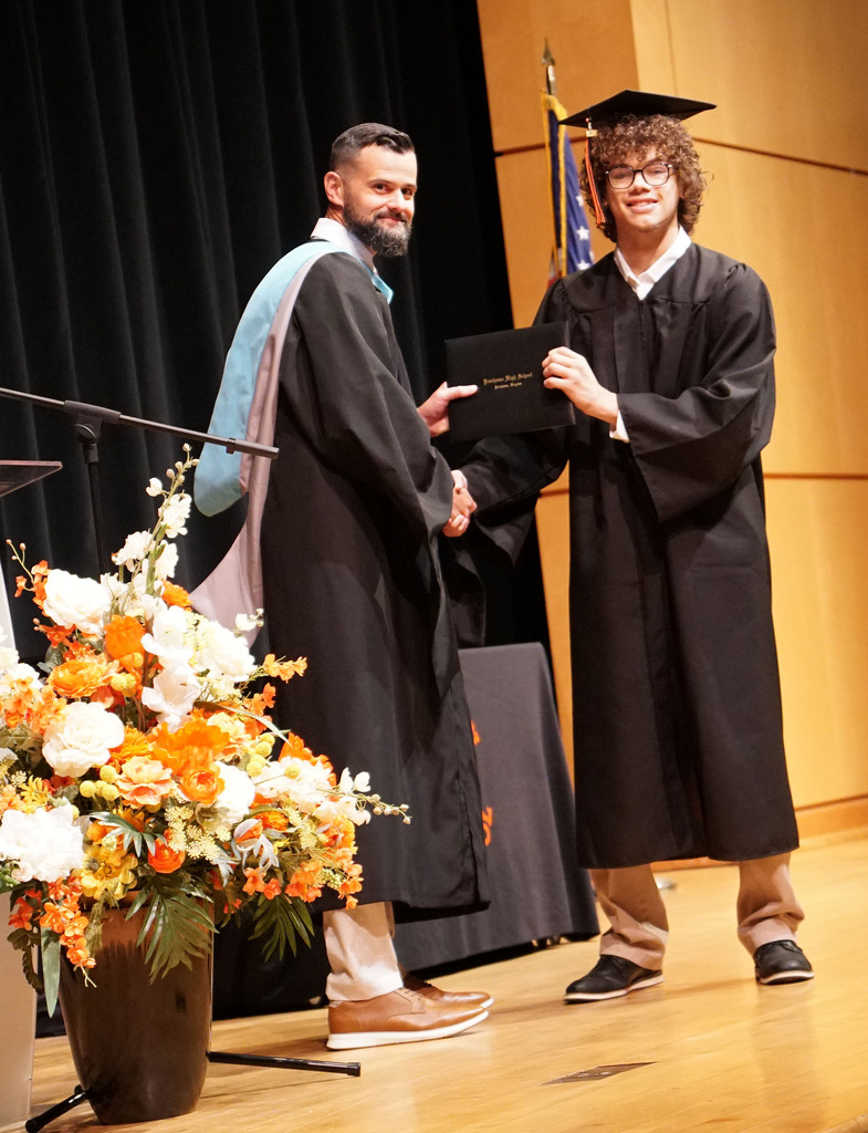 A graduate accepts his diploma from the high school principal during a summer graduation.